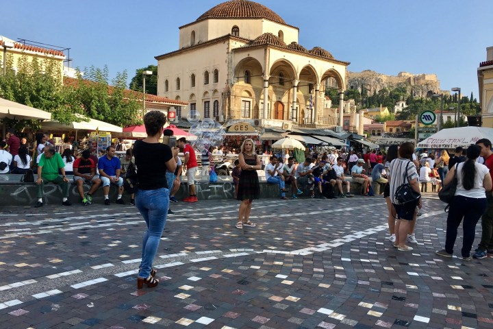 a group of people walking down the street with Monastiraki in the background